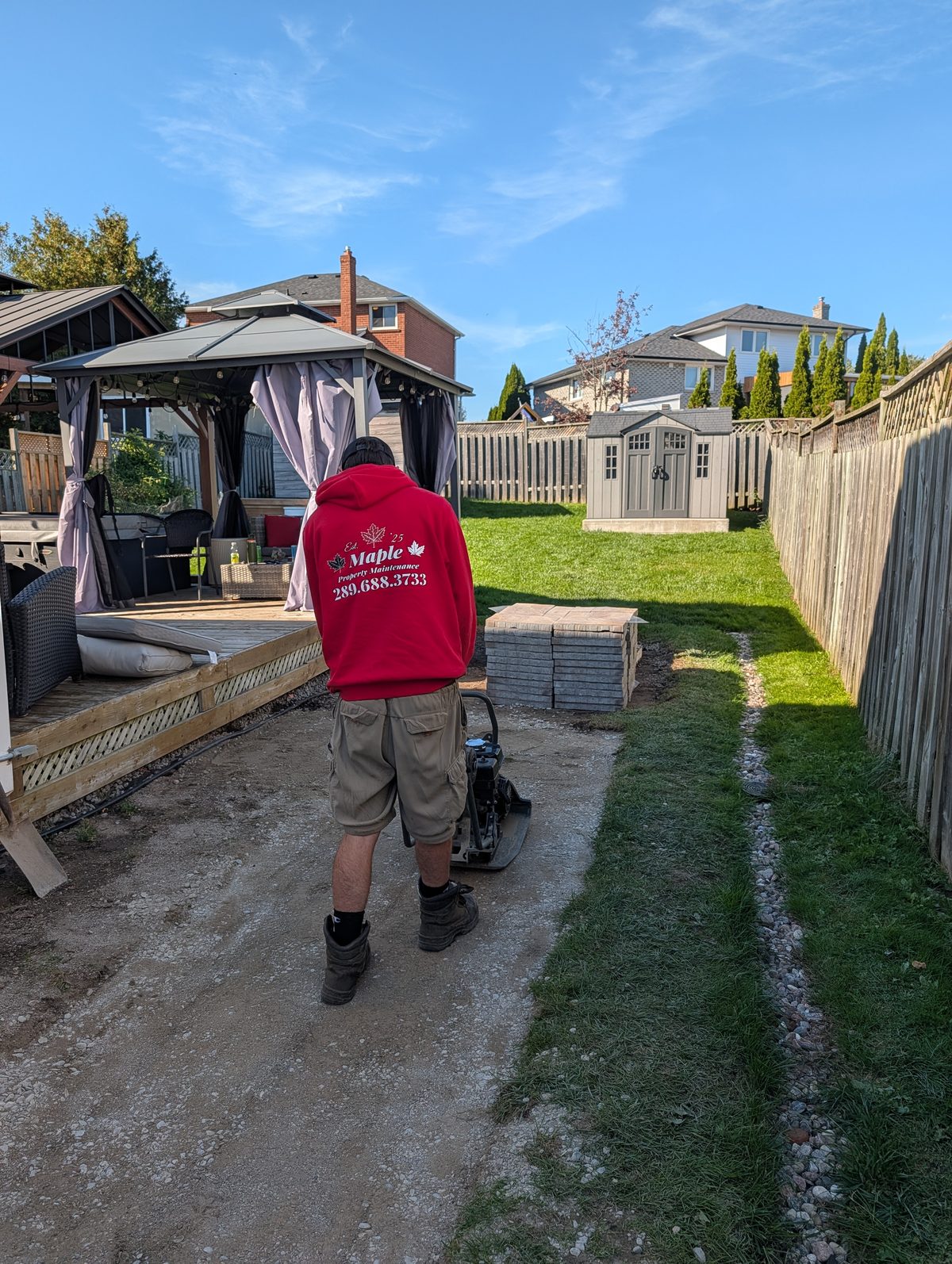 Crew member using a plate compactor to prepare a base for a backyard paver patio